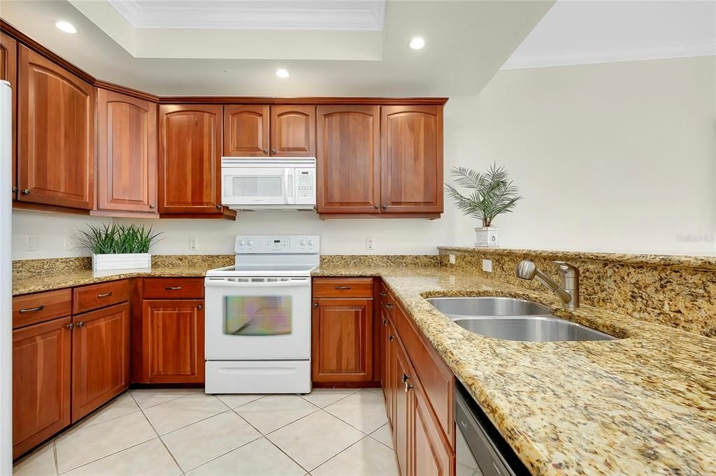 Kitchen featuring light stone countertops, ornamental molding, white appliances, and a tray ceiling