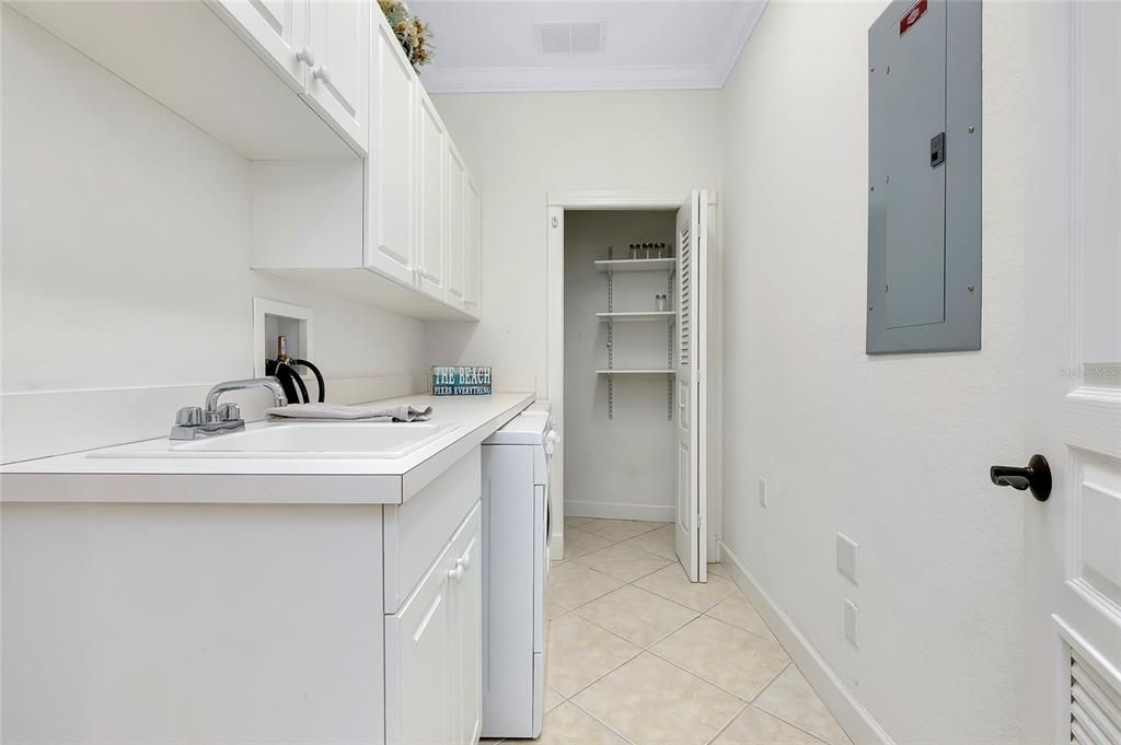 Laundry area featuring light tile patterned floors, cabinets, ornamental molding, electric panel, and sink