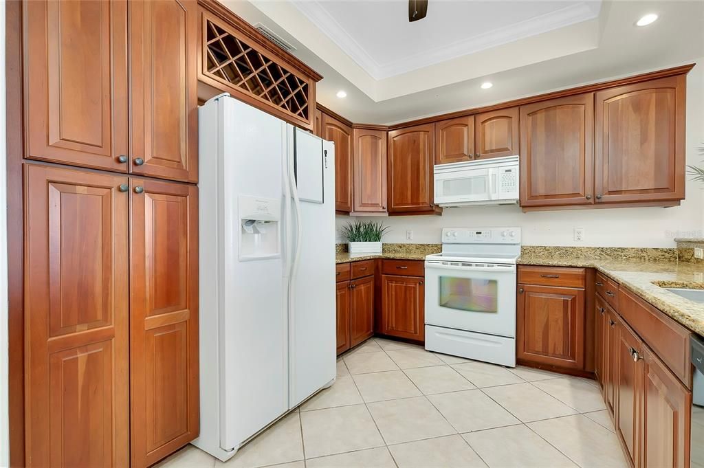 Kitchen featuring light stone countertops, ornamental molding, white appliances, and a tray ceiling