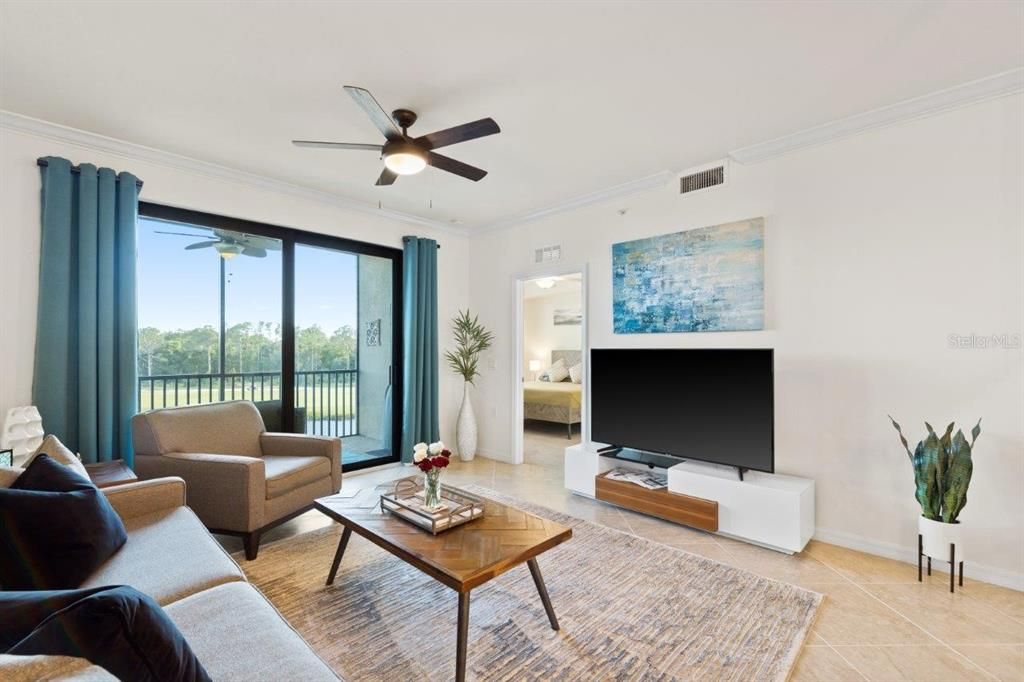 Living room featuring 16" tile, high ceilings, crown molding, and sliding glass doors leading to the covered screened-in patio.