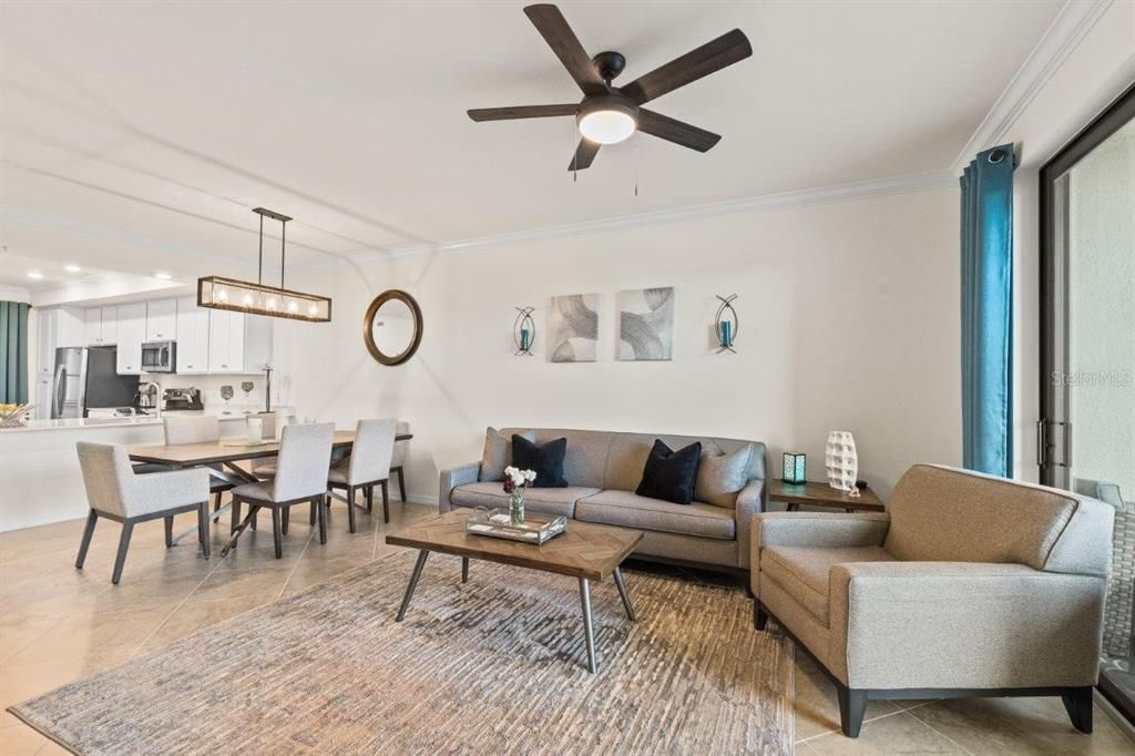 Living room featuring 16" tile, high ceilings, crown molding, and sliding glass doors leading to the covered screened-in patio.