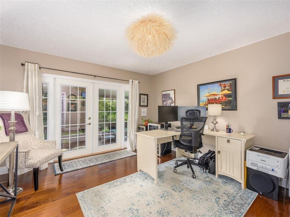 Bright and inviting home office with French doors leading to the backyard. The space offers natural light and views of greenery, providing a productive and comfortable workspace. Hardwood floors and neutral wall colors enhance the room's charm.