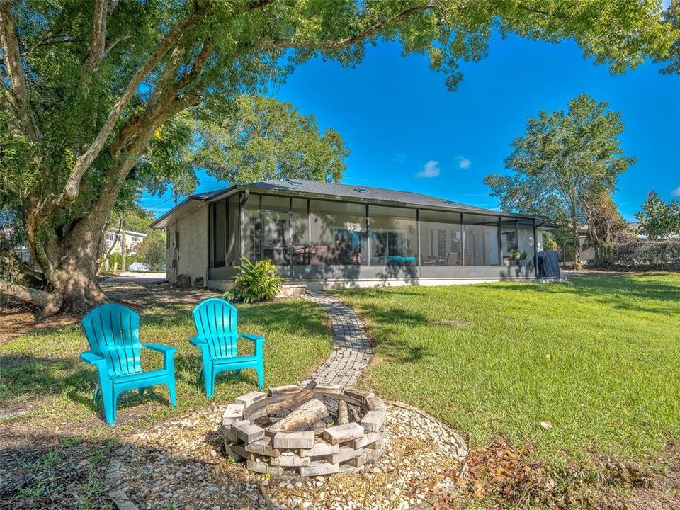 Charming backyard featuring a spacious screened patio and a cozy fire pit, perfect for outdoor entertaining or relaxing. Surrounded by mature trees, this outdoor space offers a peaceful retreat with ample shade and a well-maintained lawn.