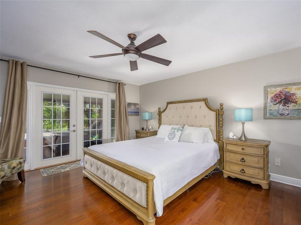 This primary bedroom boasts ample natural light with large French doors leading to the private outdoor area. High ceilings, hardwood floors, and neutral wall tones create a bright and welcoming space perfect for relaxation. The room offers plenty of space for customization and personalization.