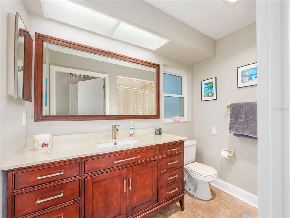 Bright and spacious primary bathroom featuring an elegant wood vanity with ample storage, a large mirror, and a sleek single sink. The neutral tones and natural light provide a clean, modern atmosphere.