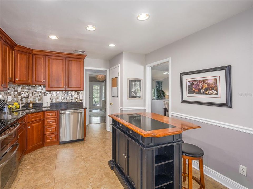 Spacious kitchen featuring elegant wood cabinetry, granite countertops, and a sleek stainless steel dishwasher. The tile flooring and modern backsplash add a polished touch. The open layout leads to additional living spaces, perfect for both casual dining and entertaining.