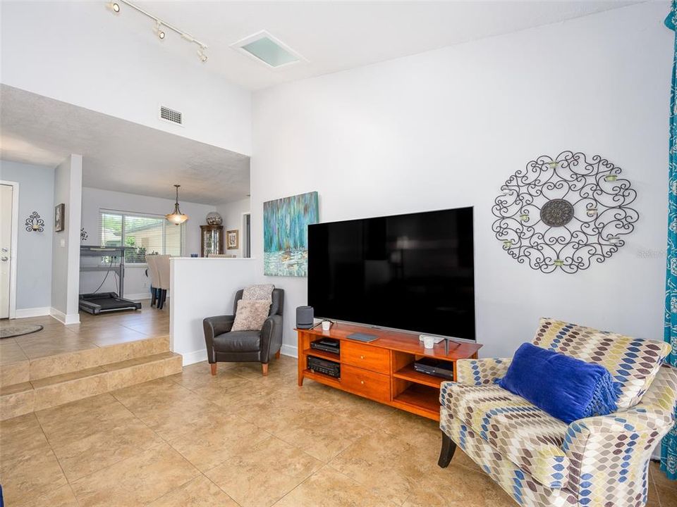 This spacious living area features high ceilings, sleek tile flooring, and natural light flowing through large windows. The open floor plan connects seamlessly with the dining area, offering a versatile layout perfect for modern living.