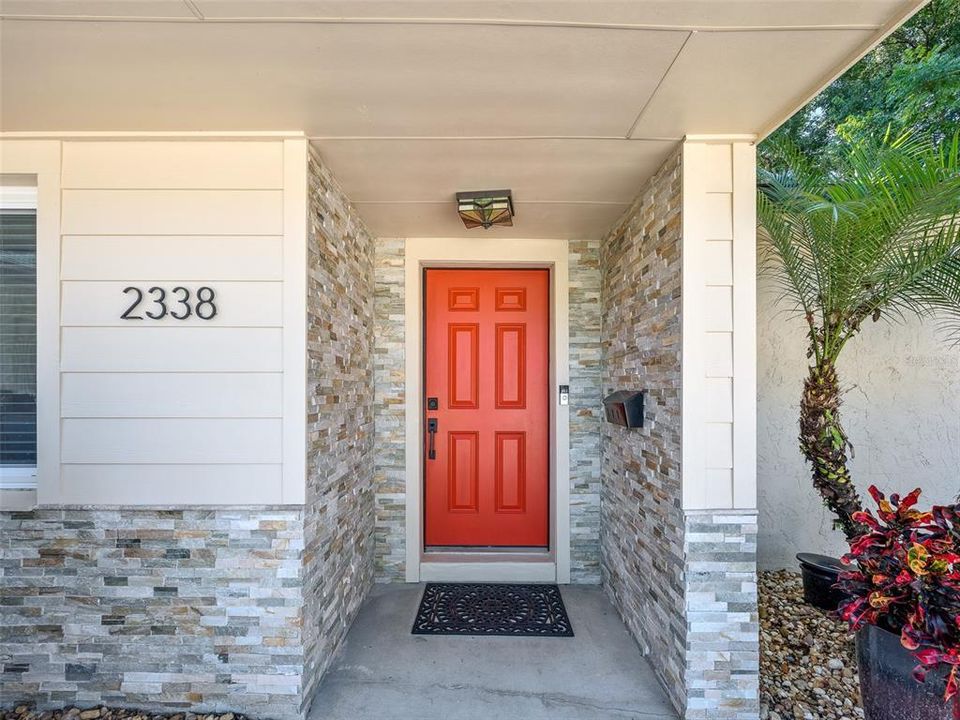 Charming front entry with modern stone accents and a bold red door, offering great curb appeal. The covered porch creates a welcoming first impression, complementing the fresh, contemporary exterior design.