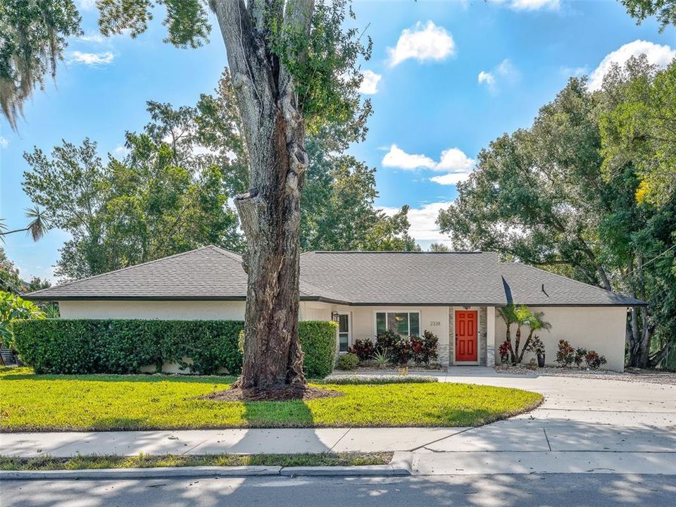 This inviting single-story home features a beautifully landscaped front yard with mature trees and well-maintained hedges. The charming red front door adds a pop of color, and the large driveway offers ample parking. Perfect curb appeal for a cozy residence.