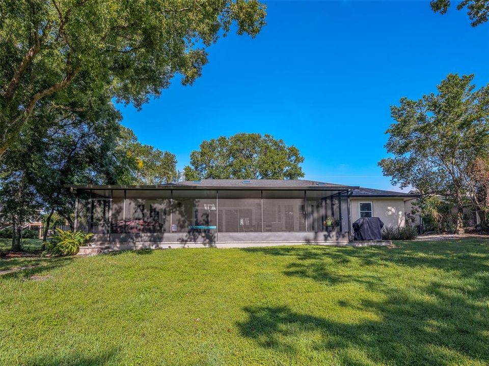 Expansive backyard with mature trees providing ample shade, perfect for outdoor activities. The large screened-in patio offers a versatile space for entertaining or relaxation, enhancing the indoor-outdoor living experience. A serene and spacious setting ideal for enjoying Florida living.