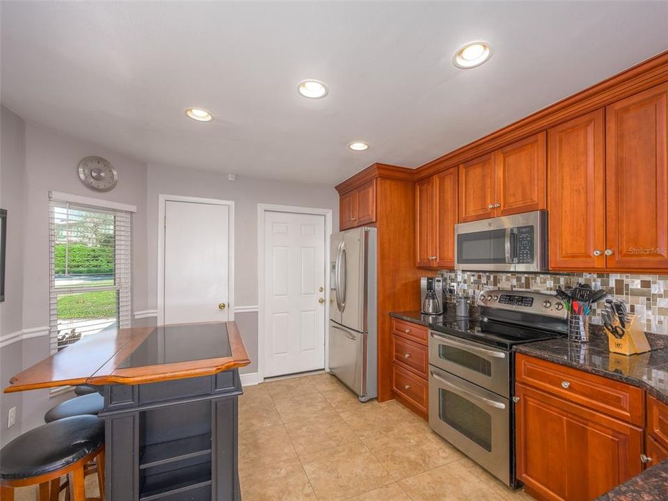 This bright, updated kitchen offers modern stainless steel appliances, rich wood cabinetry, and a spacious layout perfect for cooking and entertaining. Ample natural light flows through the window, highlighting the sleek granite countertops and tile flooring for a clean, timeless look.