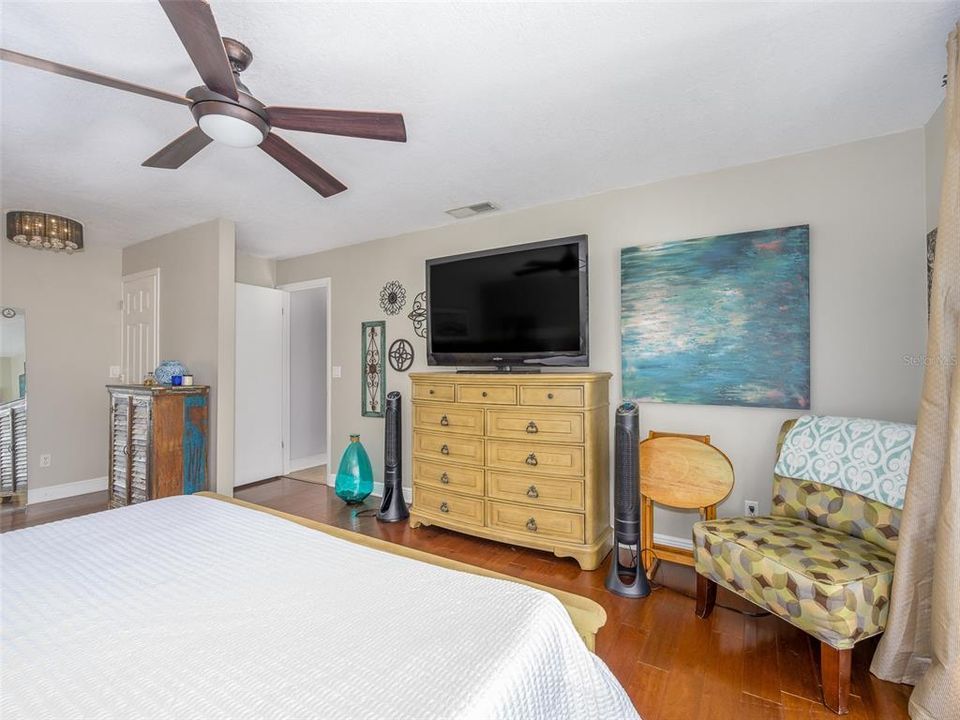 Spacious bedroom with natural light and hardwood floors, offering a versatile layout. The neutral paint tones create a calming atmosphere, perfect for personalizing the space. Ample wall space for large art or media setups. Ceiling fan provides comfort and air circulation.