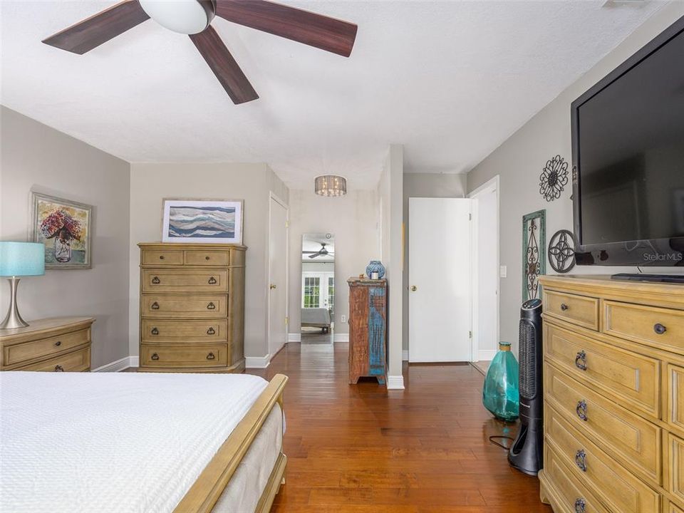 Spacious bedroom featuring rich hardwood floors, neutral wall tones, and ample natural light. The room flows seamlessly into the hallway, enhancing the open feel. Ceiling fan and closet space add functionality, making this room move-in ready.