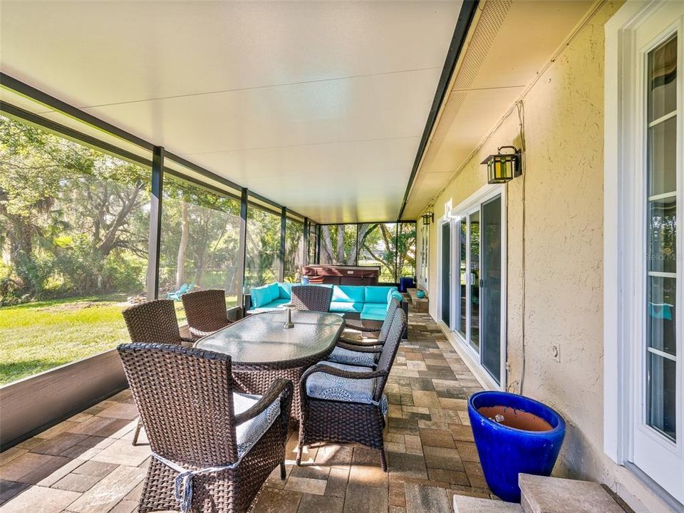 Spacious screened-in patio with a hot tub, outdoor dining area, and comfortable seating, perfect for relaxing while enjoying serene views of the surrounding greenery and lake.