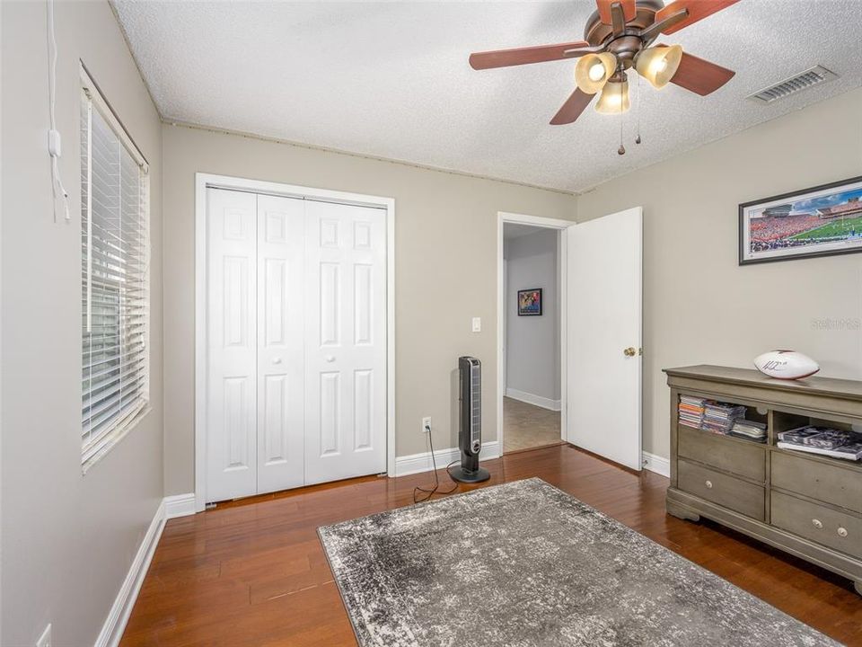 This bedroom offers ample natural light, hardwood floors, and neutral wall tones, creating a comfortable and inviting space. A ceiling fan enhances airflow, while a large closet provides plenty of storage. Ideal for personal retreat or guest room use.