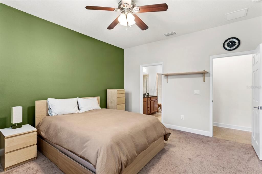 Spacious primary suite with neutral carpet and ceiling fan