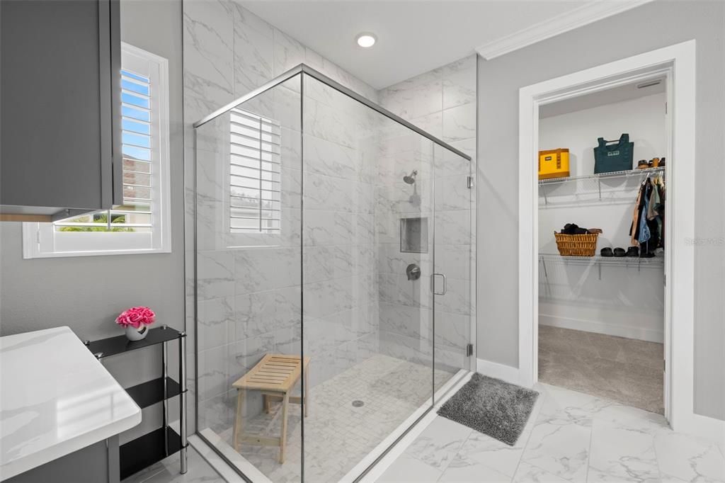 Primary En-Suite Bath Includes a Sizable Tiled Shower with Frameless Glass Doors & Storage Nook