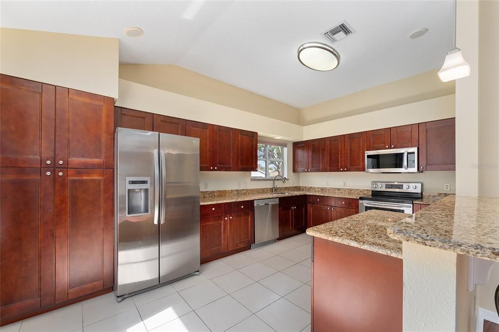 KITCHEN has plentiful SHAKER STYLE cabinets w/ PULL OUTS & built in PANTRY and GRANITE COUNTERTOPS. Note PENDANT LIGHTING over BREAKFAST BAR.