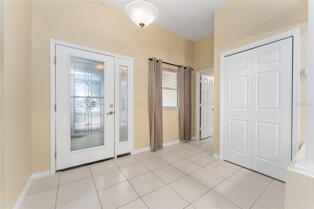 View of FOYER shows full length LEADED GLASS front door (L) & coat closet (R). Entrance to LAUNDRY ROOM visible (far R).