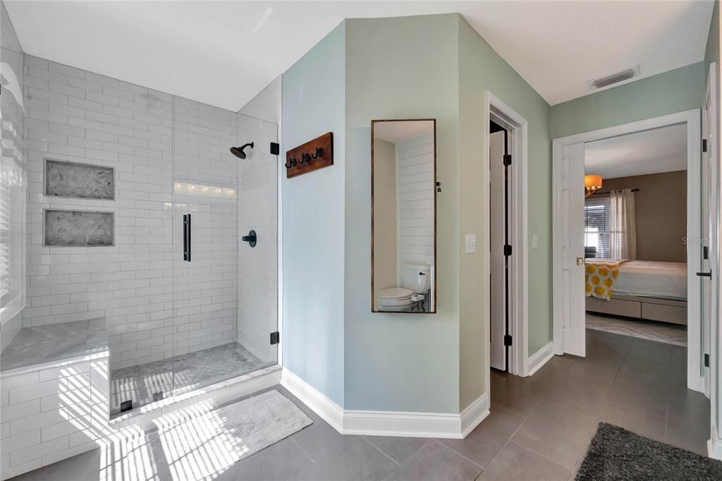 Start and end your day in style, this private bath has a DUAL SINK VANITY with complementary hardware and decorative lighting on a shiplap accent wall and an oversized WALK-IN SHOWER with bench seating behind seamless glass.