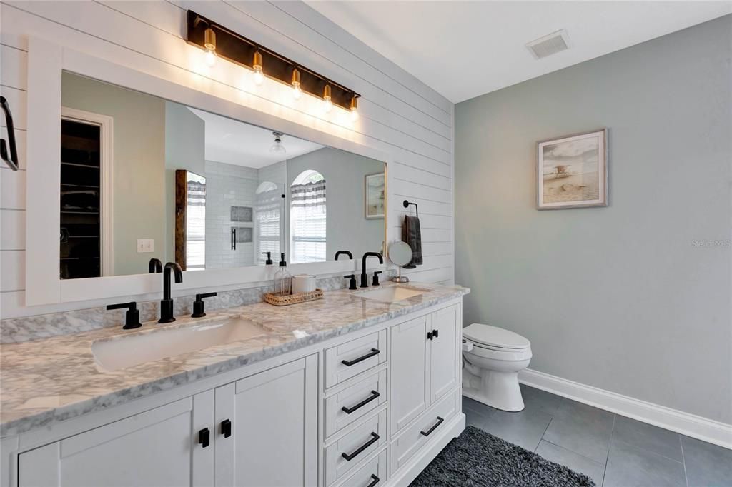 Start and end your day in style, this private bath has a DUAL SINK VANITY with complementary hardware and decorative lighting on a shiplap accent wall and an oversized WALK-IN SHOWER with bench seating behind seamless glass.