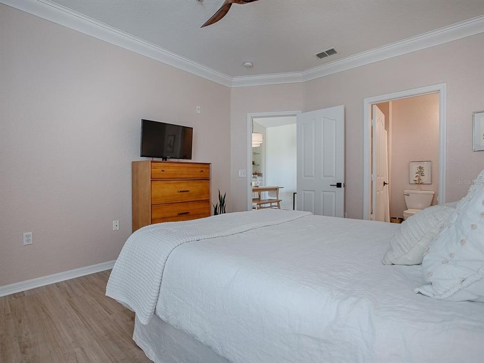 Primary Bedroom featuring new Luxury Vinyl Plank Flooring, New Ceiling Fan, New Paint, Crown Molding, Walki-in Closet and an en-suite Bathroom.