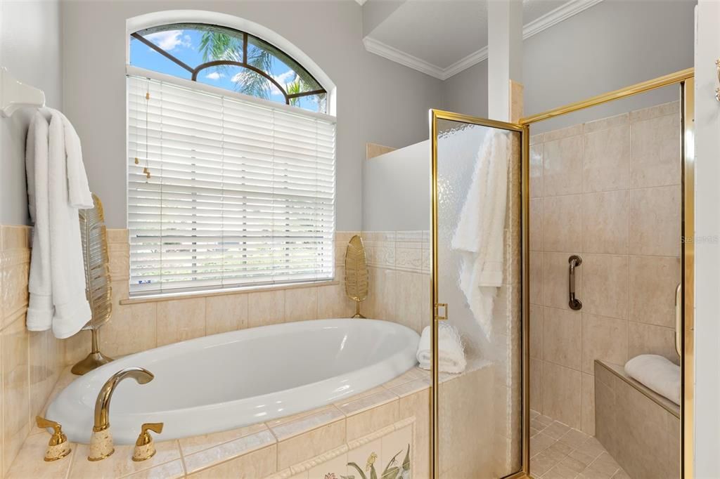 Primary ensuite bathroom with his and her walk-in closets, soaking tub, stand up shower, water closet, his and her vanity, decorative tile, and linen closet.