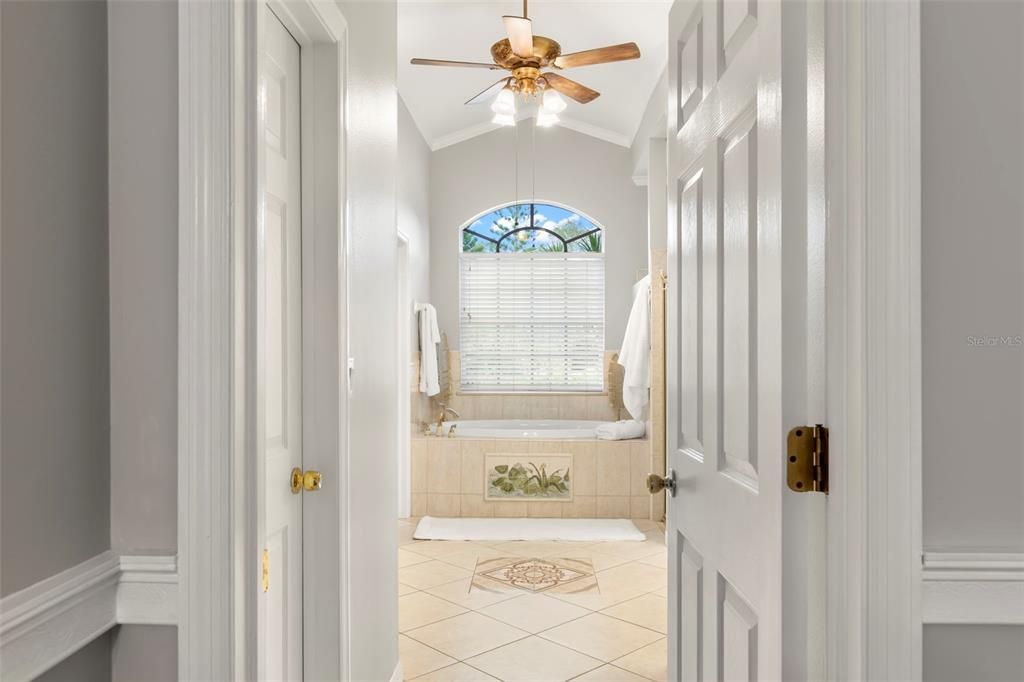 Primary ensuite bathroom with his and her walk-in closets, soaking tub, stand up shower, water closet, his and her vanity, decorative tile, and linen closet.