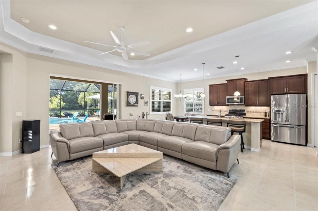 Large great room featuring tray ceilings, crown molding, modern tile, and plantation shutters.