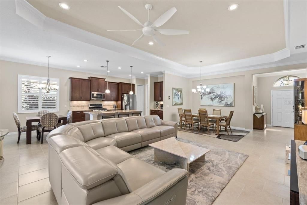 Large great room featuring tray ceilings, crown molding, modern tile, and plantation shutters.