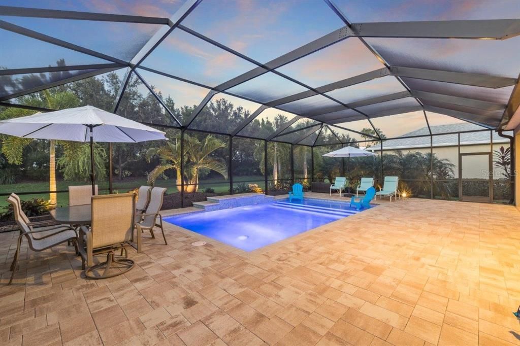 Huge screened-in lanai featuring paver floors, a new 2022 heated self cleaning pool, and a cover sitting area.