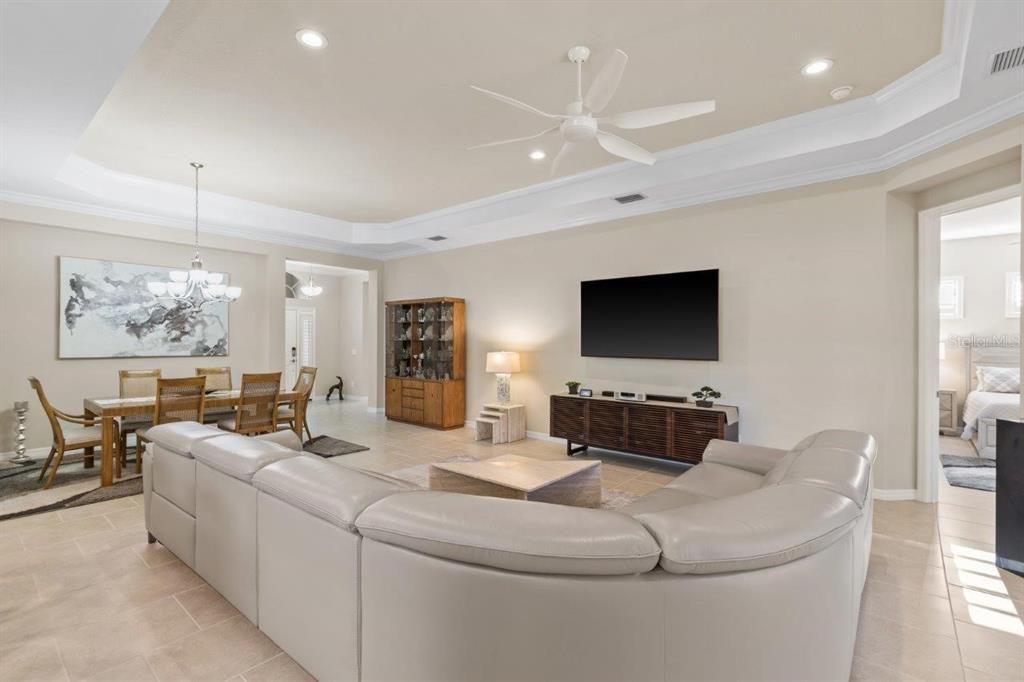 Large great room featuring tray ceilings, crown molding, modern tile, and plantation shutters.