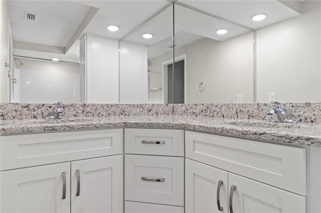 Primary bath with double sinks, wood cabinets, and granite