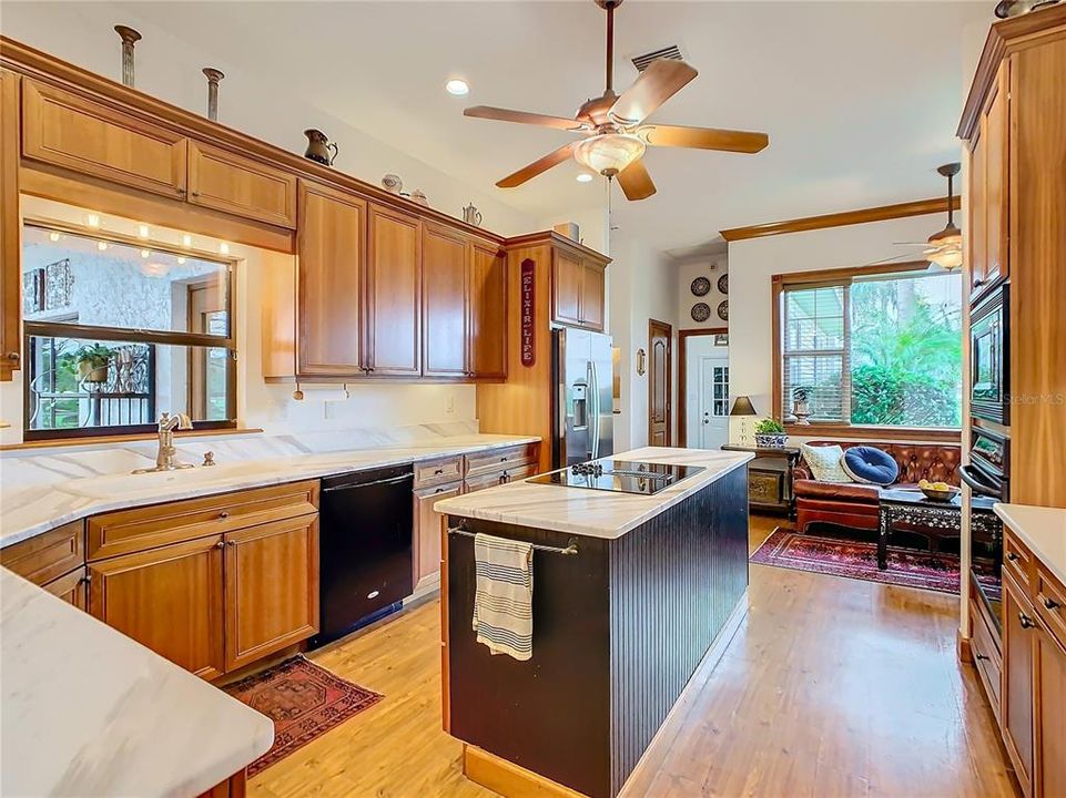 The kitchen is a chef’s delight and boasts beautiful wood cabinets, marble counter tops, center island with cooktop, a breakfast bar and a window over the kitchen sink that looks out to the pool.