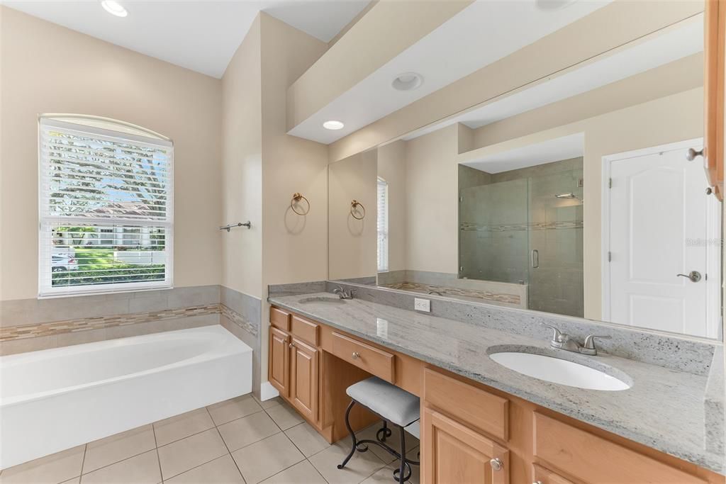 Primary bathroom has a large jetted tub and vanity area with dual sinks and granite counters.