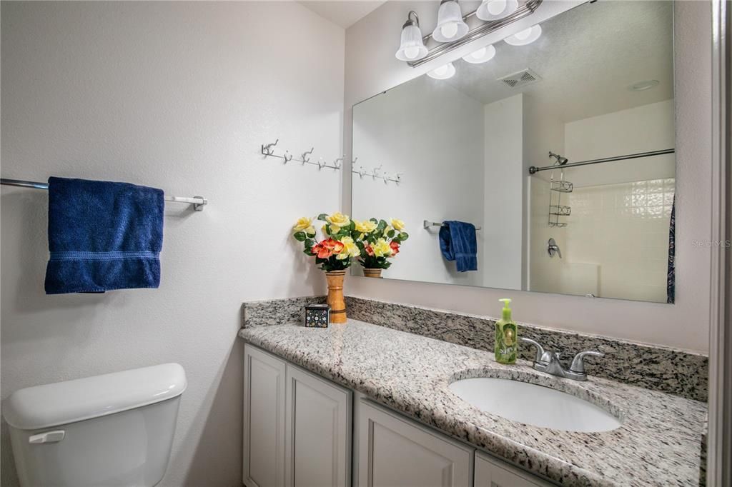 A single sink vanity with granite countertops and ceramic tile flooring.