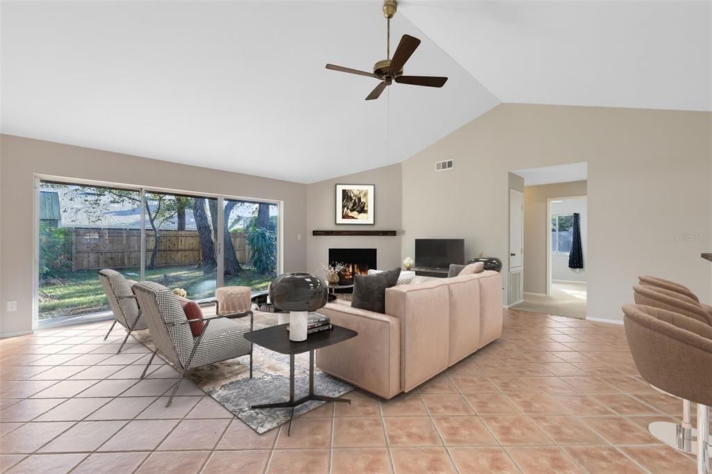 This photo has been virtually stage. This space boasts a soaring vaulted ceiling, a cozy wood-burning fireplace, and sliding glass doors that lead to a covered lanai