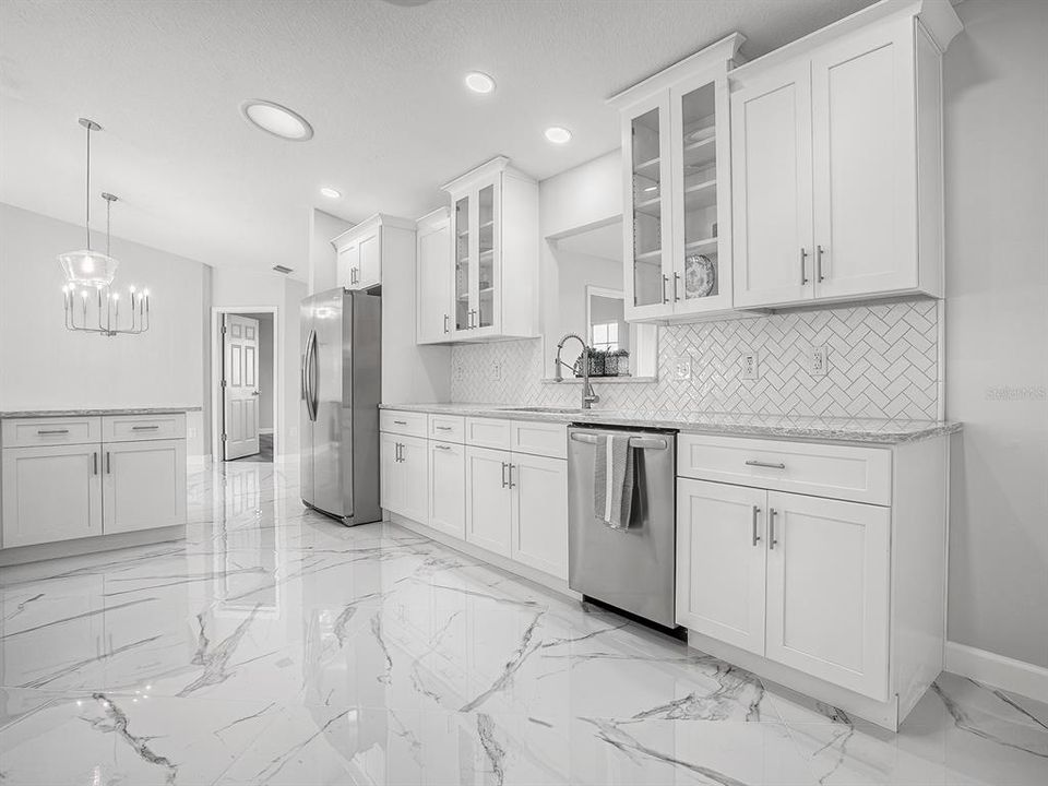 Newly renovated Kitchen featuring 32" Porcelain Tile Flooring, Staggered White Shaker Cabinets, Quartz Countertop, Stainless Steel Appliances, Recessed & Pendant Lighting and Custom Tiled Backsplash