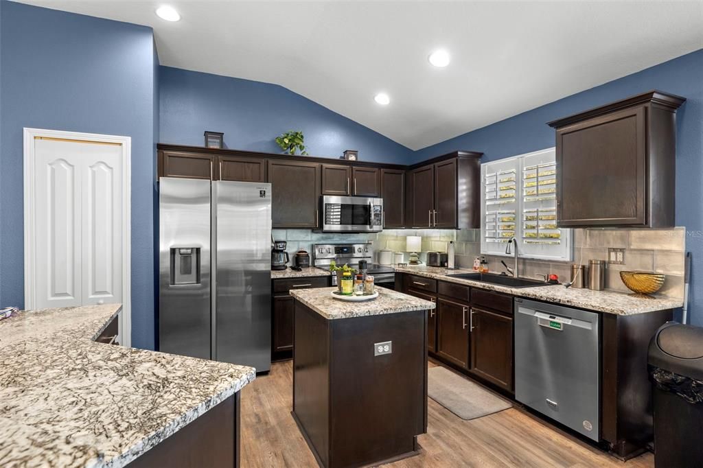 Granite counters, Espresso-stained cabinets and stainless steel cabinets provide for a well positioned layout for the home chef. The white door on the left is the pantry.