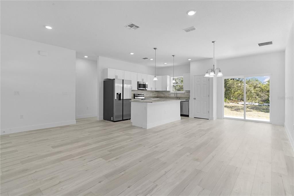 From front corner of living room, looking at the dining area on the right and kitchen center. Doorway to bedrooms 2 and 3 just left of the refrigerator