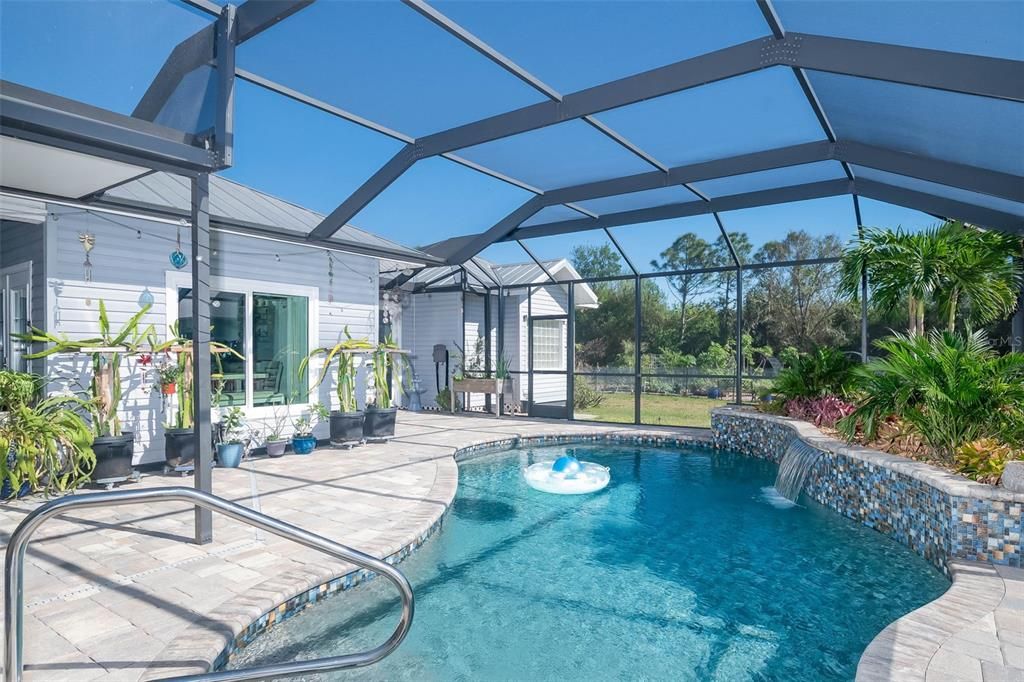 Pool area has tiled pavers and a beautifully colored garden wall