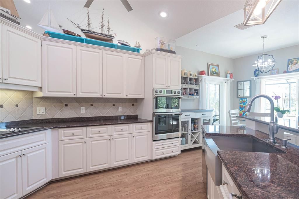 beautiful backsplash tile, a farmhouse sink with a gooseneck faucet, dual ovens, and designer lighting over the breakfast bar granite top island.