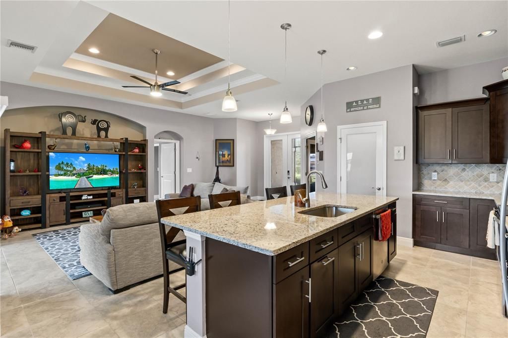 Kitchen with ceiling fan, sink, a kitchen island with sink, light stone countertops, and decorative backsplash