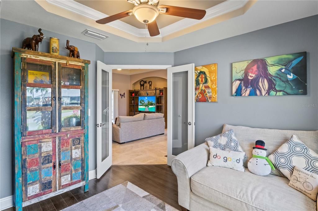 Living room featuring ceiling fan, a raised ceiling, crown molding, and wood-type flooring