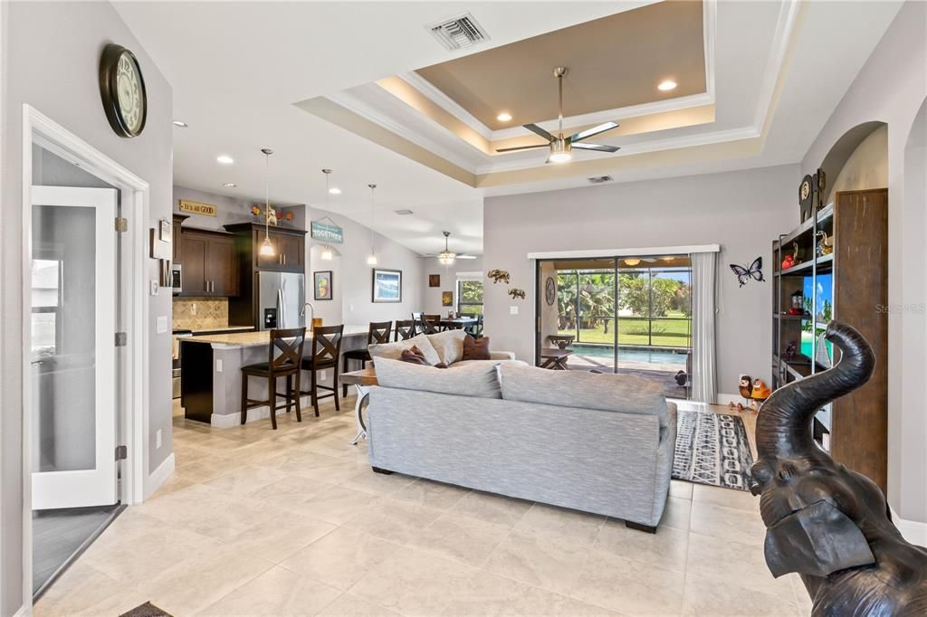 Living room with ceiling fan, a raised ceiling, and ornamental molding