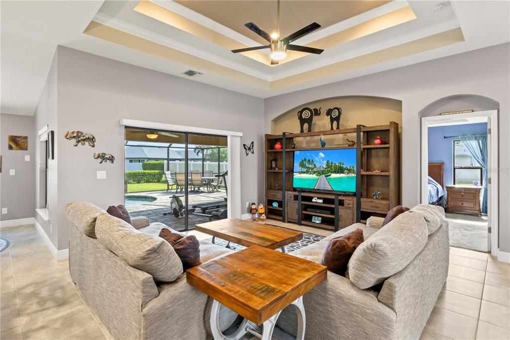 Living room with a raised ceiling, ornamental molding, ceiling fan, and a wealth of natural light