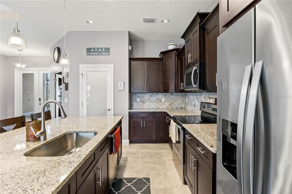 Kitchen featuring pendant lighting, light stone counters, appliances with stainless steel finishes, and sink