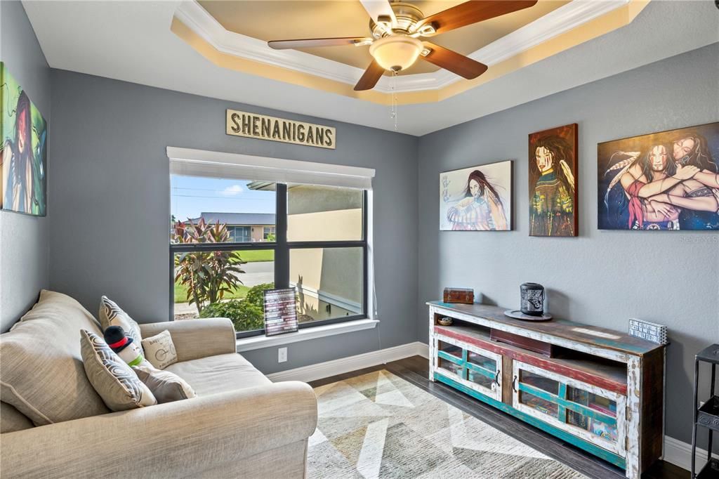 Living room with ornamental molding, wood-type flooring, a tray ceiling, and ceiling fan