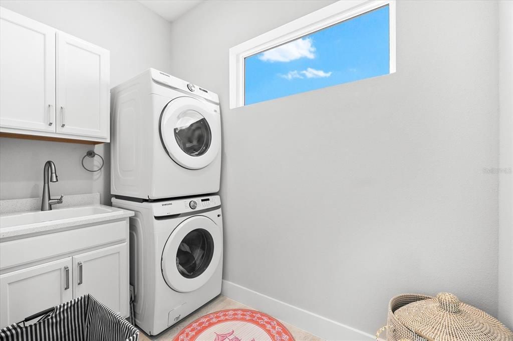 Laundry room with utility sink and stacked washer/dryer.