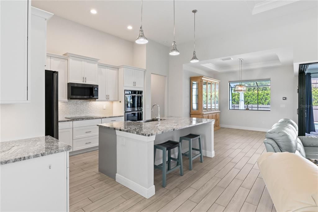 Kitchen with appliances with stainless steel finishes, light stone countertops, light hardwood / wood-style flooring, and a kitchen island with sink